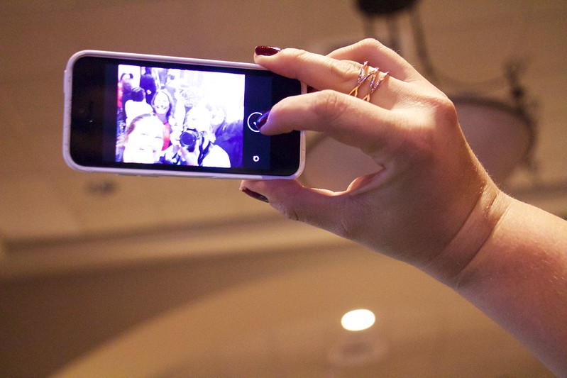 Hand die ein Smartphone hält und gerade ein Selfie schießt mit nicht erkennbaren Gesichtern.